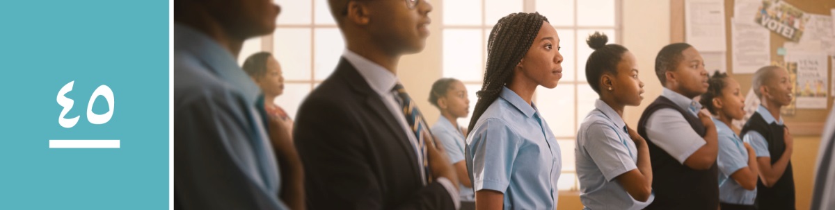 الدرس ٤٥:‏ تلاميذ يغنون النشيد الوطني ويضعون يدهم على قلبهم،‏ وأخت شابة تقف باحترام بينهم لكنها لا تغني النشيد او تفعل مثل رفاقها