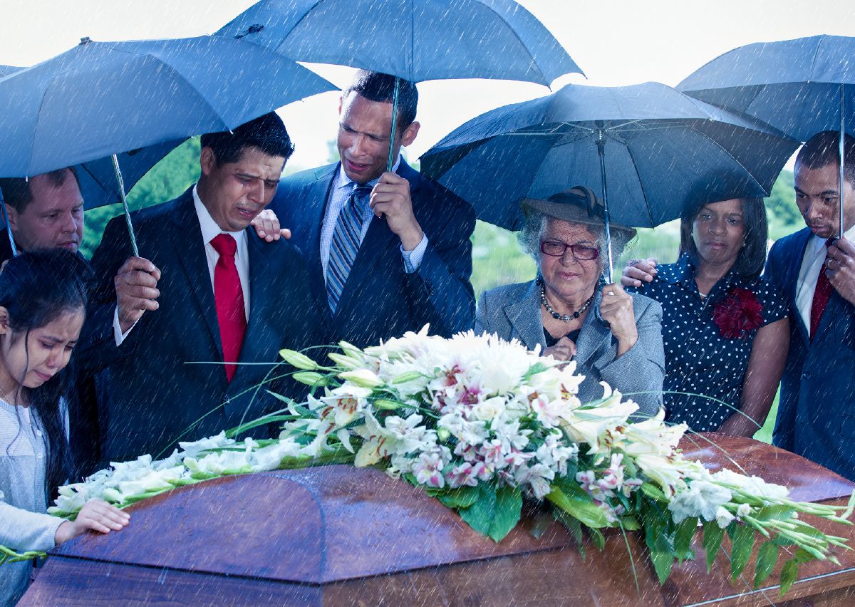 A grieving family surrounds a coffin adorned with flowers