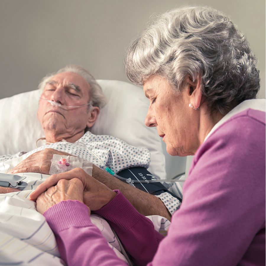 A distraught sister prays beside her husband’s hospital bed