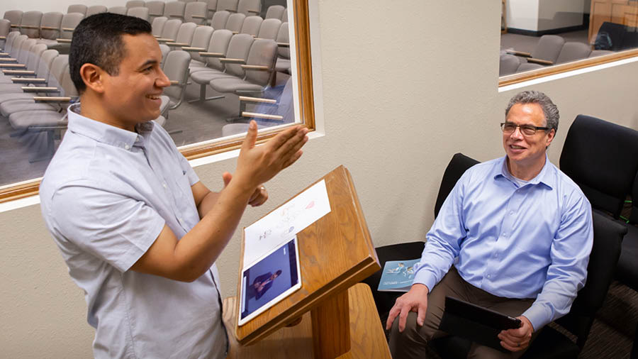 An elder listening to a brother practice a talk. The elder holds an open “Teaching” brochure.