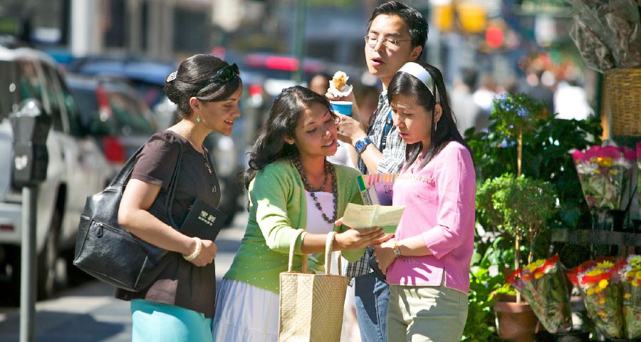 Deux sœurs prêchent à une jeune femme dans la rue. Un jeune homme regarde par-dessus leur épaule pour savoir de quoi elles parlent.