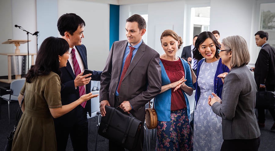 At a Kingdom Hall, local publishers surround a visiting couple and ask questions.