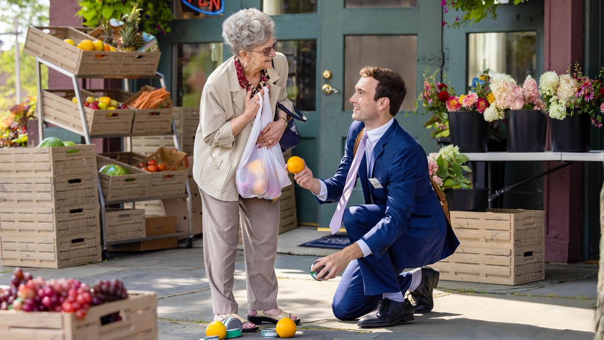 A brother helping an elderly woman by picking up some groceries that have fallen out of her shopping bag.