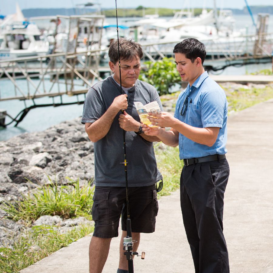 Un hermano predicando en un puerto deportivo; le está mostrando un tratado a un pescador.