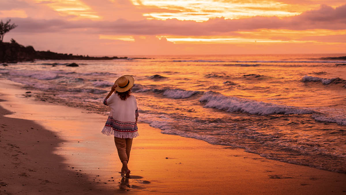 Una germana observant la posta de sol i les onades que trenquen a la vora del mar mentre camina per la platja.