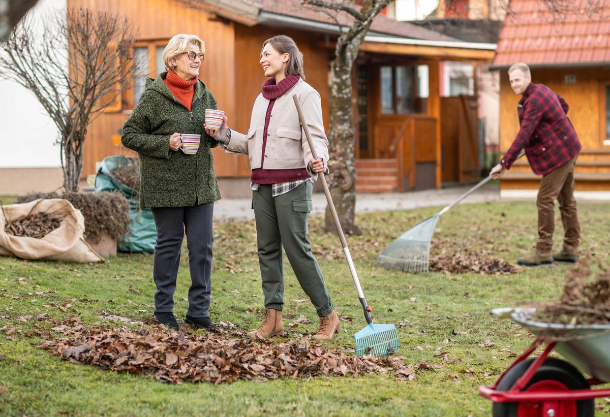 Et ægtepar hjælper en ældre kvinde med at rive blade sammen i hendes have. Hun kommer med en kop kaffe til dem.