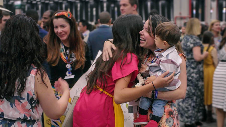 Eine Szene aus dem Video „Internationale Kongresse 2019: ‚Die Liebe versagt nie!‘“. Auf einem internationalen Kongress umarmen sich Delegierte und einheimische Brüder und Schwestern und heißen einander willkommen.