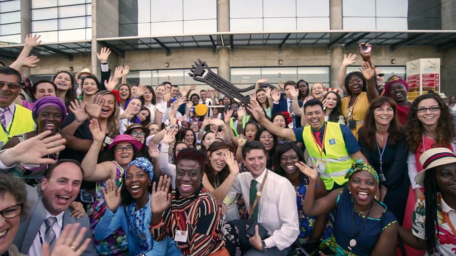 Eine Szene aus dem Video „Internationale Kongresse 2019: ‚Die Liebe versagt nie!‘“. Einheimische Brüder und Schwestern posieren zusammen mit Delegierten für ein Gruppenfoto.