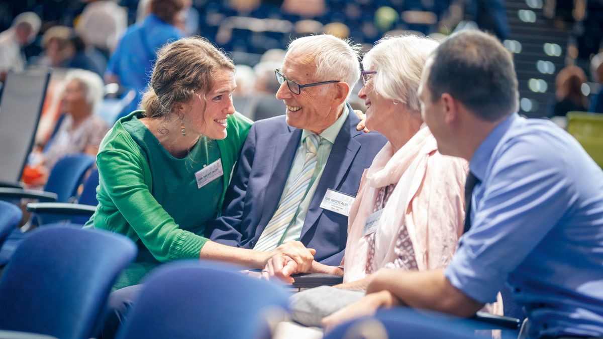 Ein junges Paar unterhält sich bei einem regionalen Kongress freudig mit einem älteren Ehepaar.