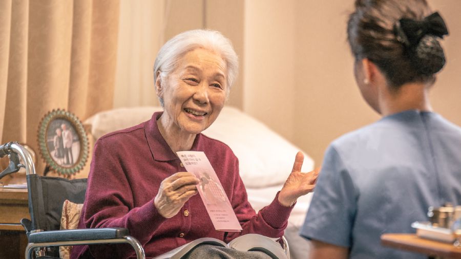 Eine ältere Schwester im Rollstuhl bietet einer Krankenpflegerin ein Traktat an