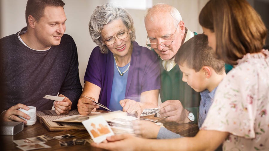 Ein Ehepaar sieht sich Fotos an und blickt zusammen mit der erwachsenen Tochter und deren Familie auf schöne Erinnerungen im Dienst Jehovas zurück