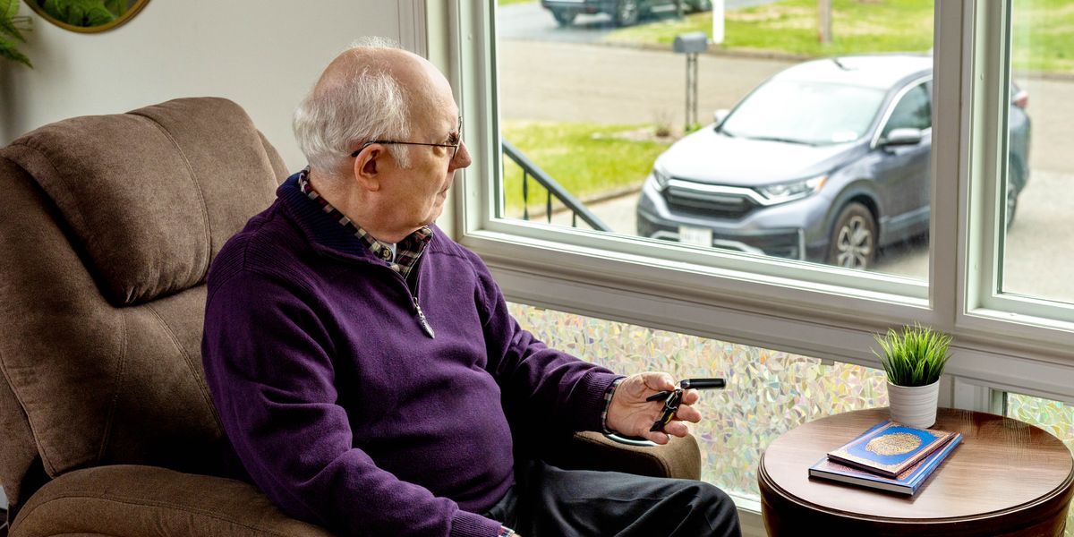 Ein älterer Bruder sitzt am Fenster und schaut auf sein Auto. Er hält seinen Autoschlüssel in der Hand und denkt nach.