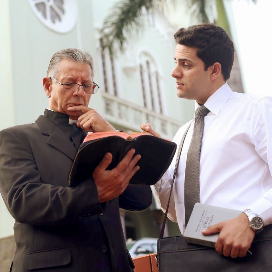 Ένας κληρικός κοιτάζει προσεκτικά ένα εδάφιο στη Γραφή του ενώ ένας αδελφός τού δίνει μαρτυρία.