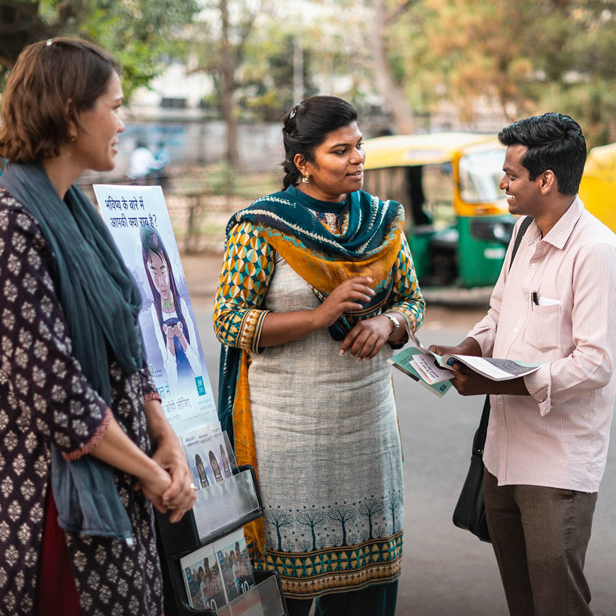 Two sisters standing next to a literature cart, preaching to a man on a street in India.