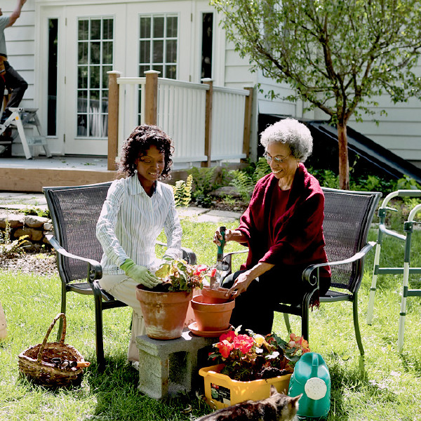 A younger sister helping an older sister plant some flowers.