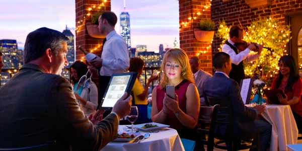A married couple dining at a restaurant use their electronic devices instead of talking to each other