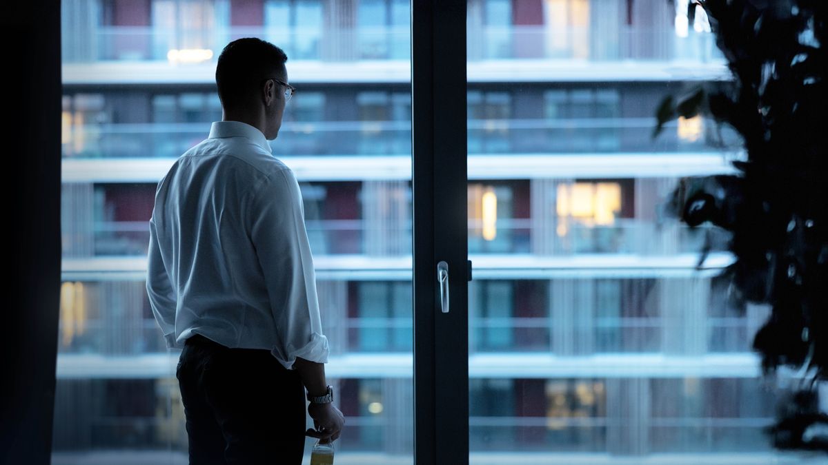A businessman stands alone, gazing out a window in the evening.