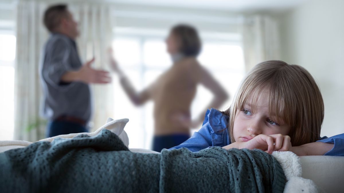 A sad young girl looking away as her parents argue nearby.