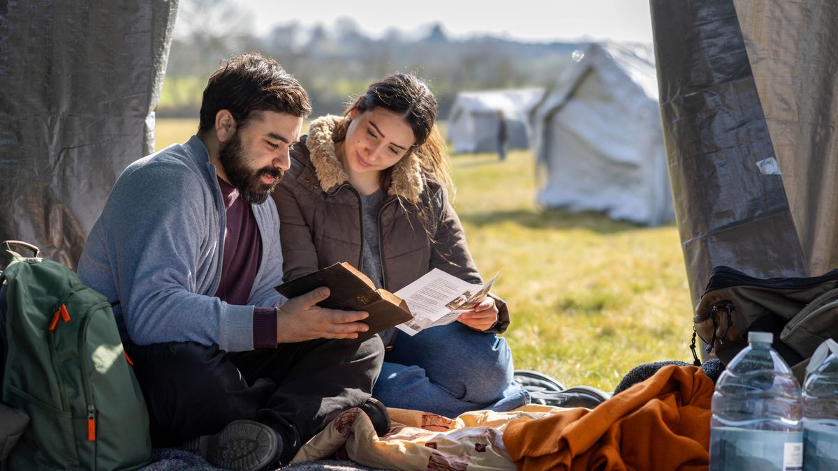 A couple reading the Bible together as they sit in their tent at a refugee camp.