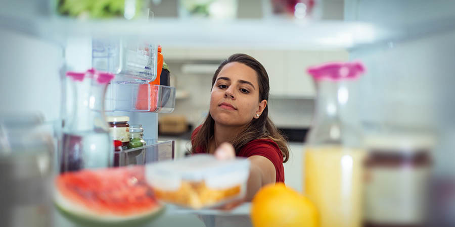 A woman storing a container of food in a refrigerator.
