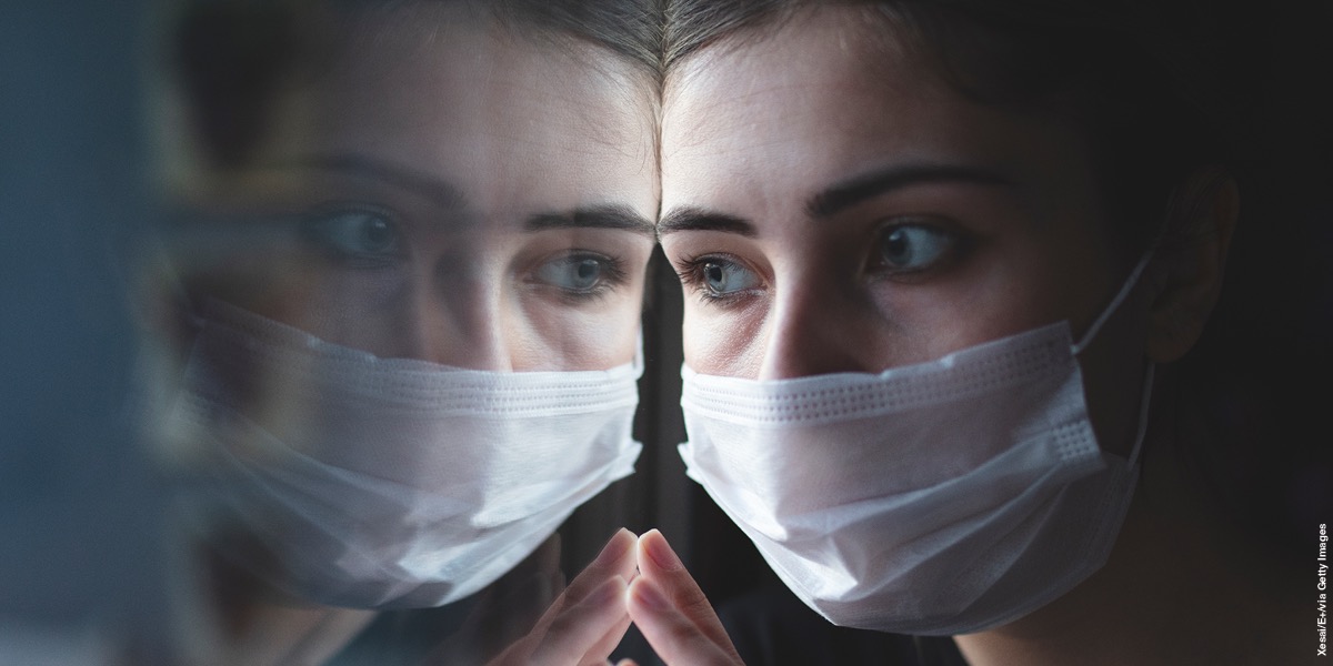 A woman wearing a face mask is looking out a window.