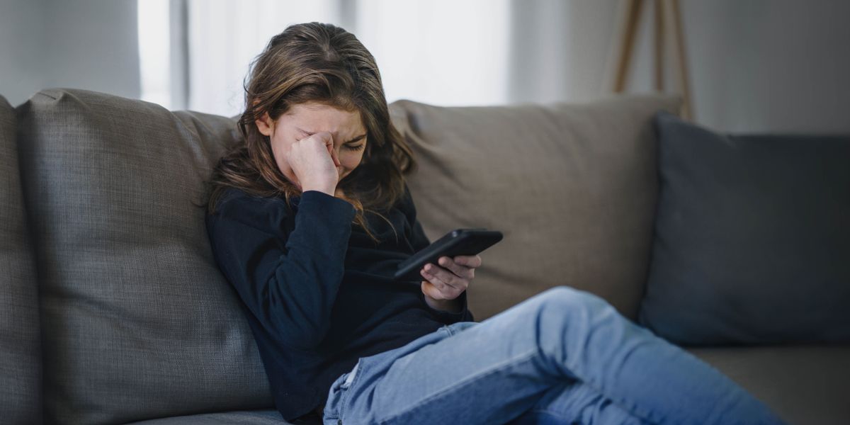 A teenage girl who is emotionally upset by what she sees on her smartphone.