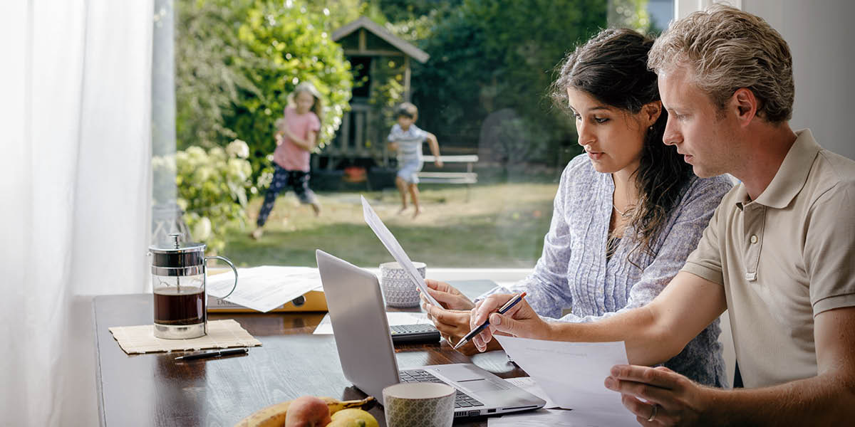 Parents discussing their finances while their children play in the backyard.