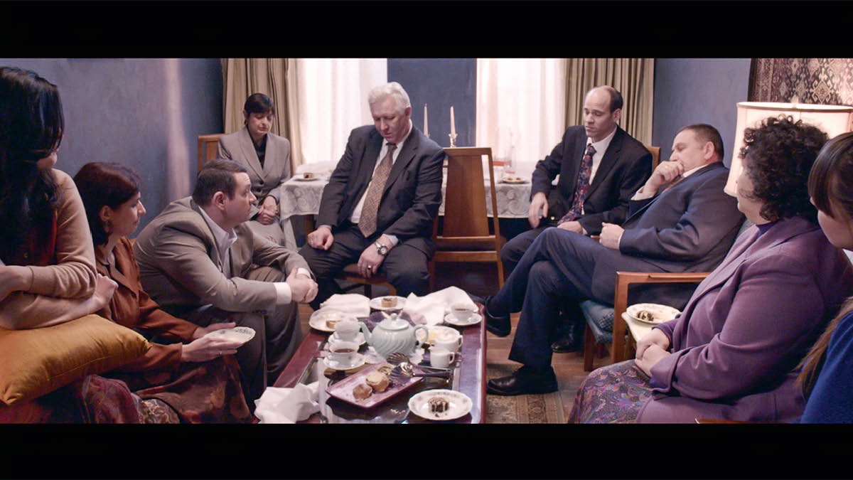 Scene from the video ‘Be Loyal, as Jesus Was​—When Praised,’ showing Sergei at a gathering in a brother’s home humbly responding to undue praise from well-meaning brothers.