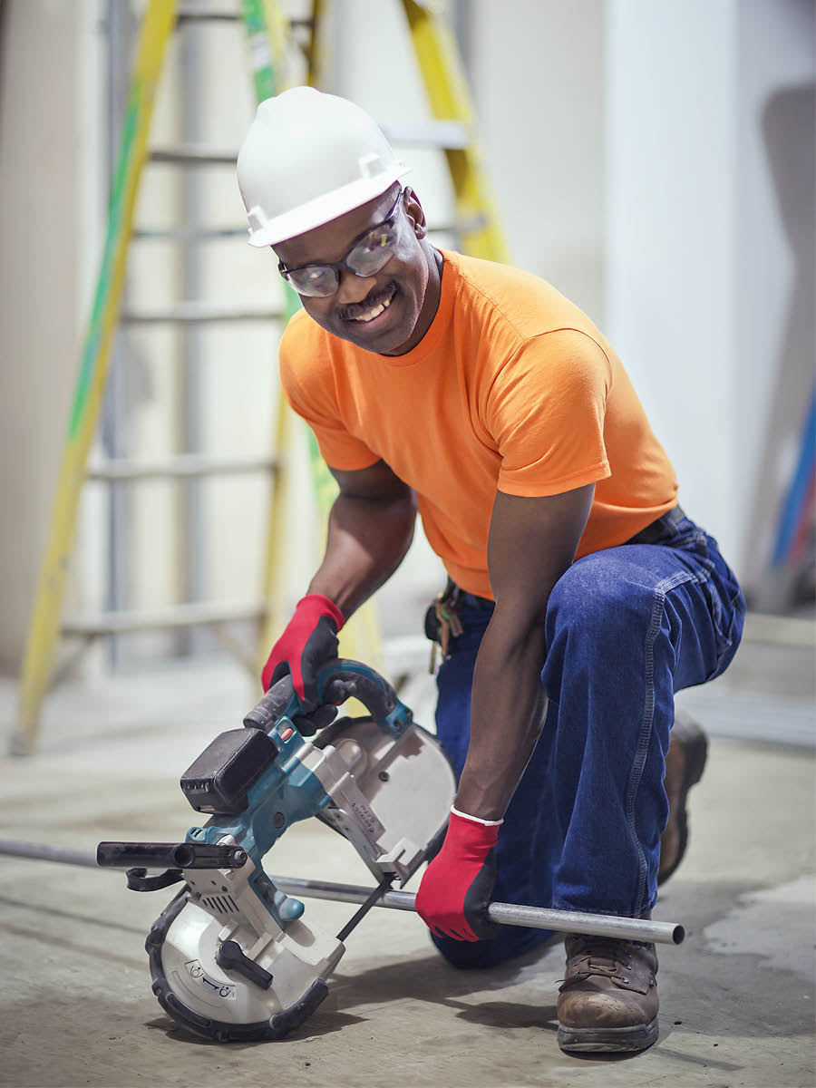 A brother smiling as he cuts metal pipe at a construction project.