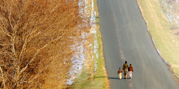 A mother and her two children walking down a road toward an unseen destination