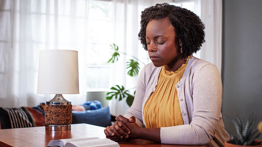 A sister sitting at a table with an open Bible as she prays.