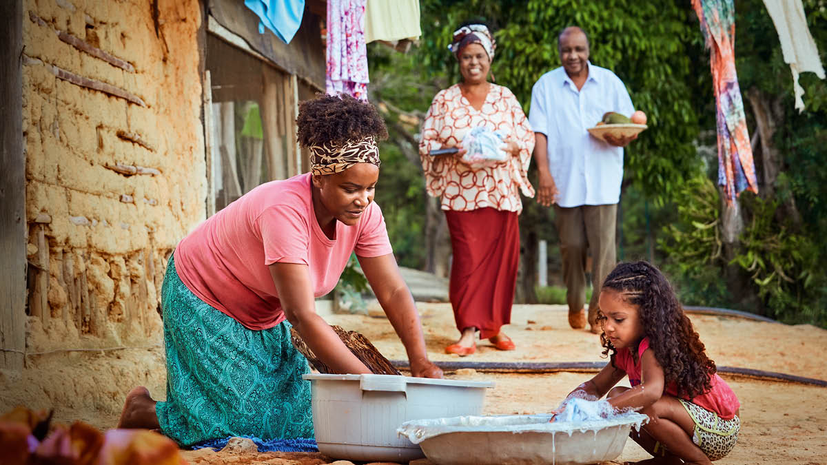A sister and her young daughter washing clothes by hand. A brother and his wife bring them a meal.