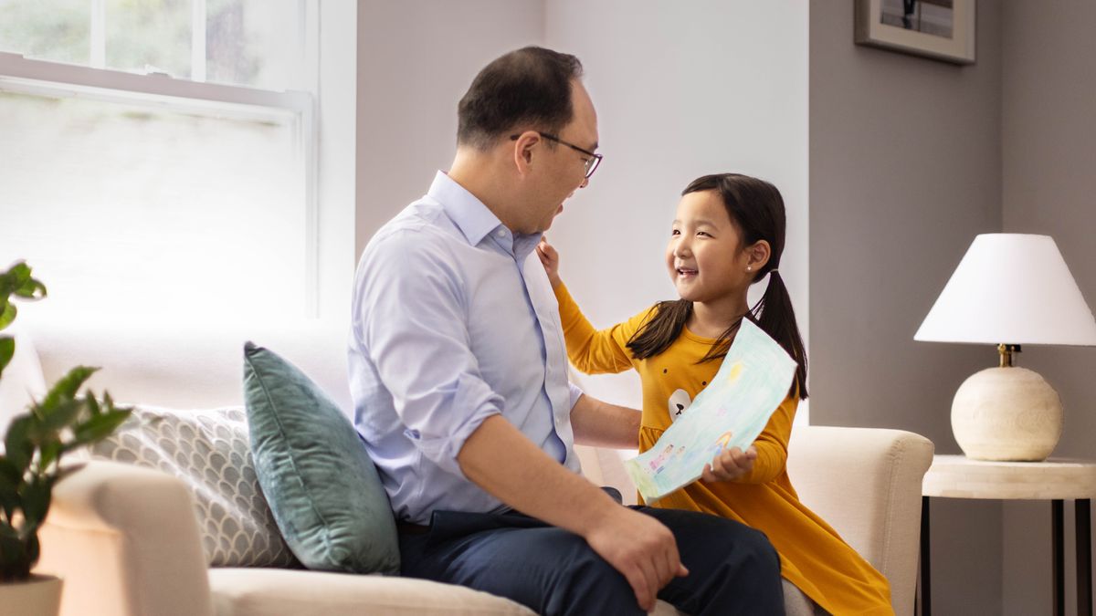 A young girl happily giving her father a drawing she made.