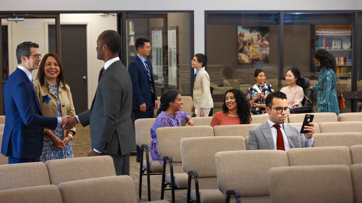 Various brothers and sisters conversing together before a meeting. One brother sits alone, looking at his cell phone.