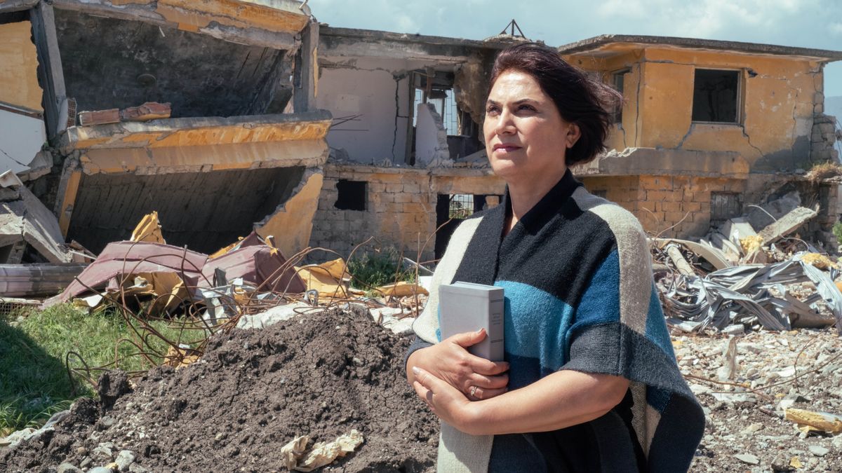 A sister holding a Bible as she stands confidently in front of a home that has been destroyed in a disaster.