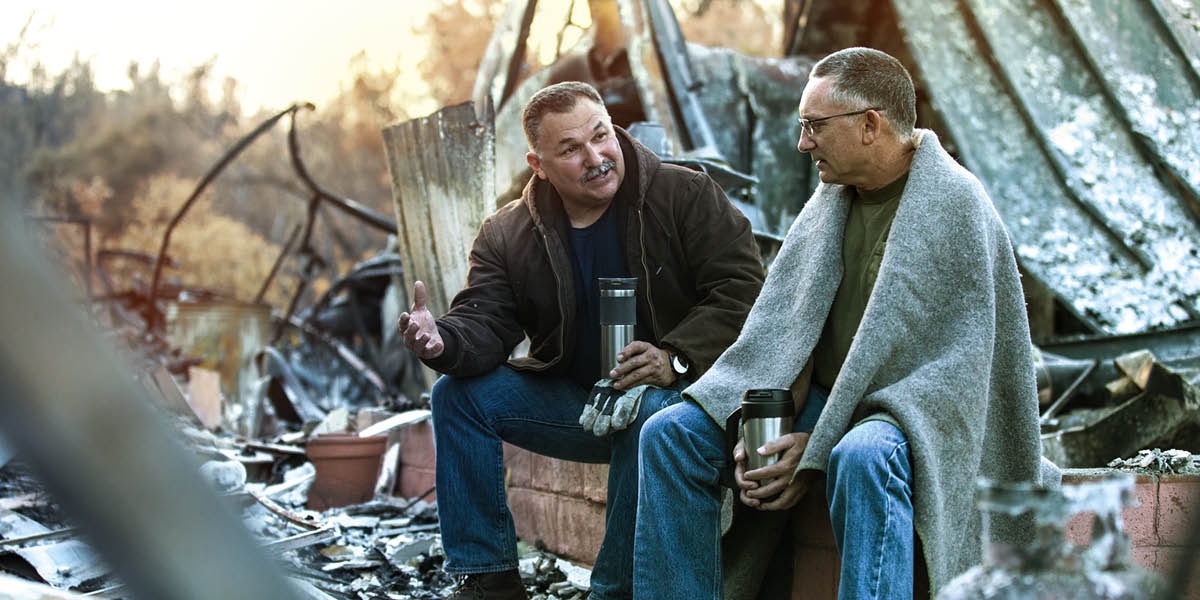 Two men sit among the rubble of a devastated building