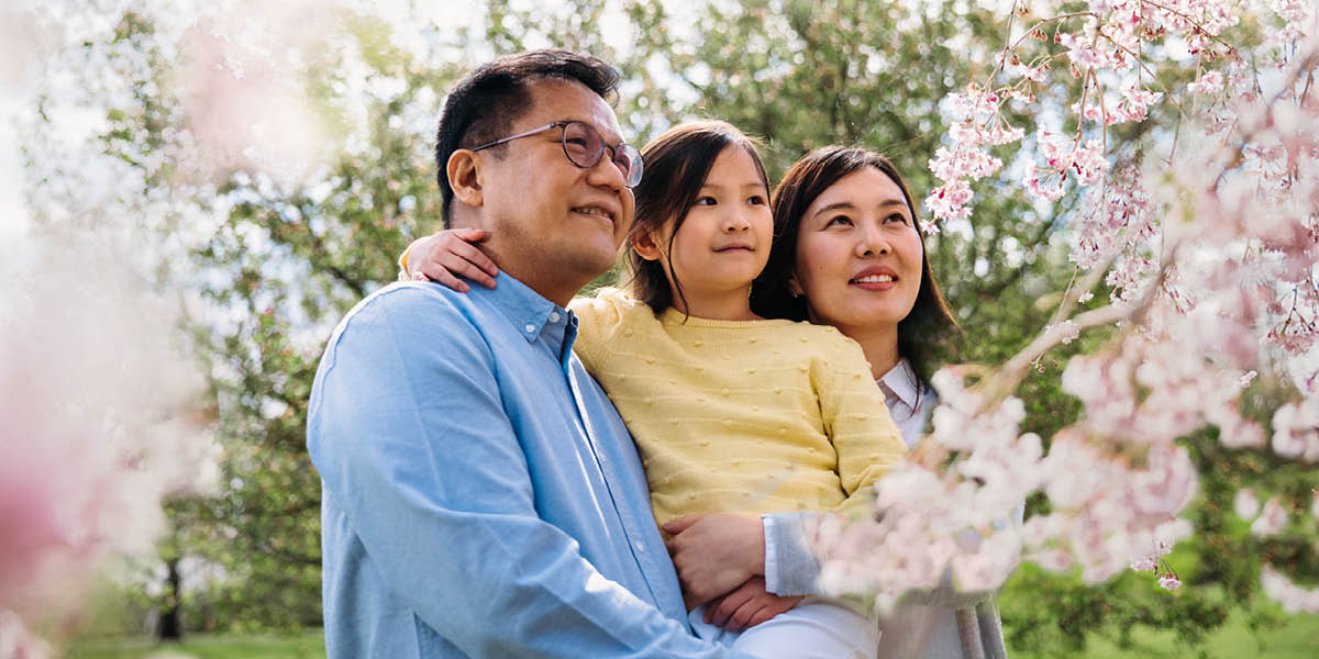 Parents with their young daughter admiring the blossoms on a cherry tree.