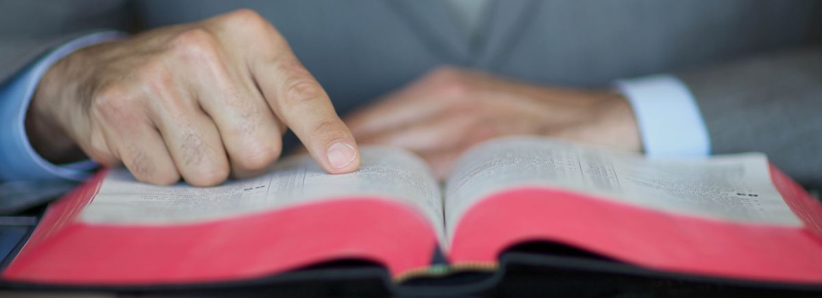 A man using his finger to follow along as he reads the Bible.