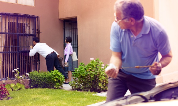 Jehovah’s Witnesses in the house-to-house ministry looking through a window as a man watches them from a distance