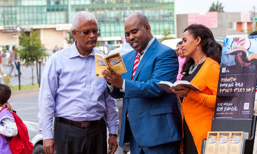 Jehovah’s Witnesses stand beside a literature cart in Addis Ababa, Ethiopia, and use Amharic literature to preach to a man