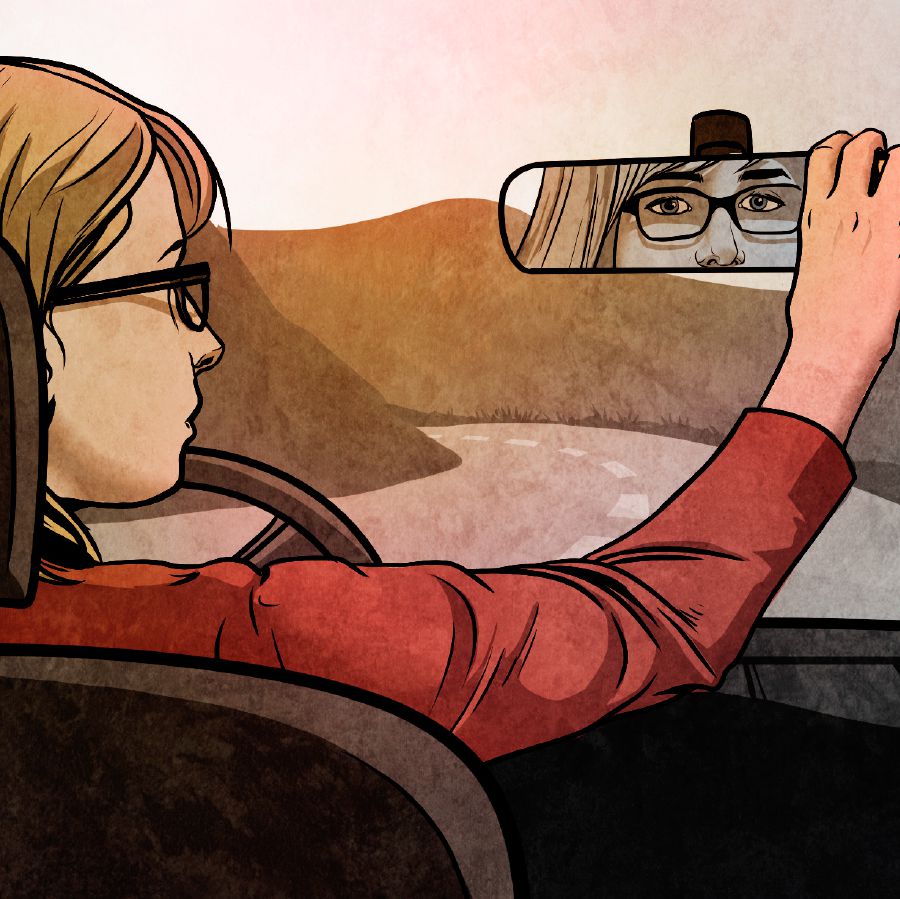 A young woman looks in a rearview mirror while driving a car