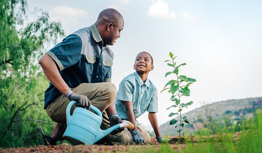 Un padre ayudando a su hijo a regar una planta