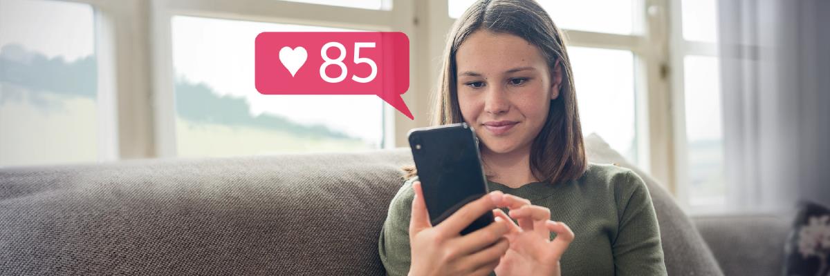 Una adolescente sonríe mientras mira su teléfono. Recibió 85 “me gusta” en una red social.