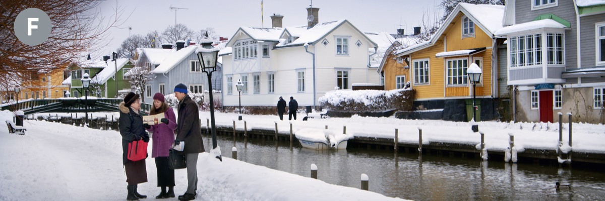F. En Suecia, dos testigos de Jehová predicándole a una mujer en una calle situada junto a un canal.