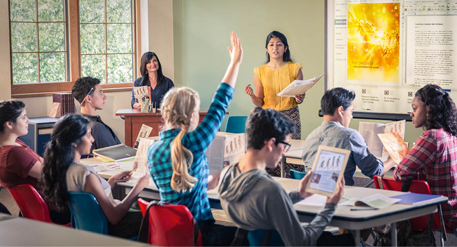 Una joven Testigo usa el folleto El origen de la vida para hacer una presentación en clase. Una compañera levanta la mano.