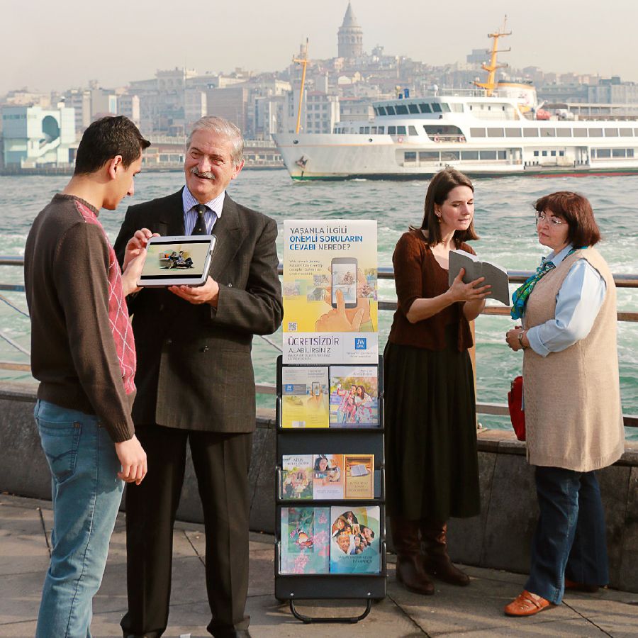 Dos testigos de Jehová predican en una zona pública con la ayuda de un exhibidor de publicaciones