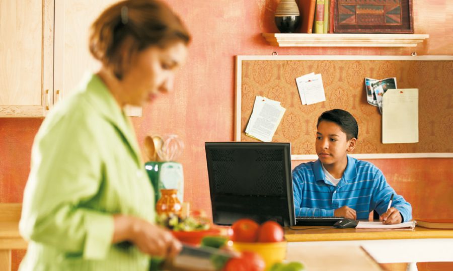 Un garçon utilise Internet dans la cuisine, pendant que sa mère prépare à manger