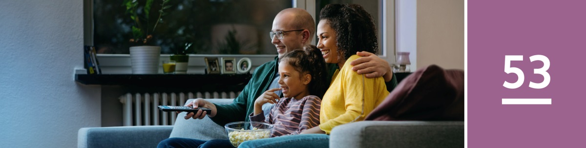 Pelajaran 53. Seorang ayah, ibu, dan anak perempuan mereka menonton TV sambil makan popcorn.