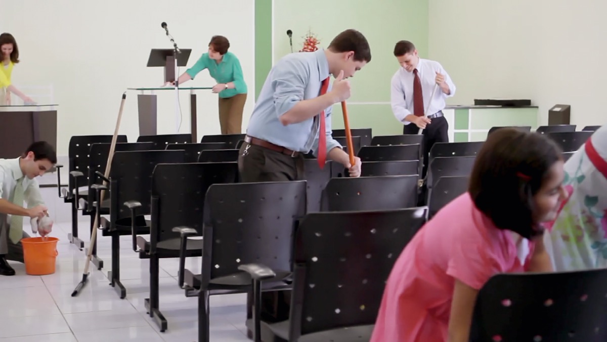 Una scena del video ‘Prendiamoci cura dei nostri luoghi di adorazione’. Uomini, donne e bambini fanno le pulizie nella Sala del Regno.