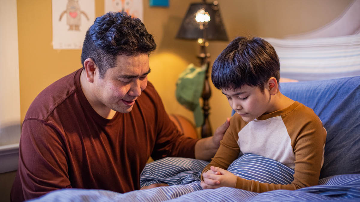 Prima di andare a dormire un papà prega insieme a suo figlio piccolo.